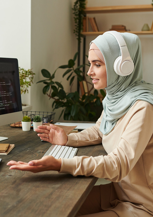 Women sitting at a desk engaging in a video call with shelves in the background.