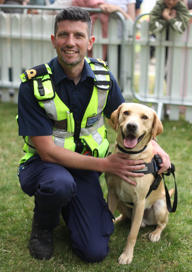 Dog handler wearing a customs officer uniform kneeling down beside a customs sniffer dog.